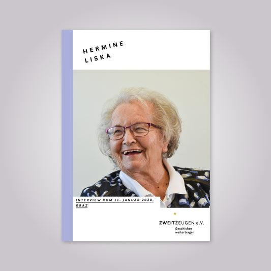 Eine alte Frau mit grauem Haar lächelt. Sie trägt eine weinrote Brille und eine gemusterte Bluse mit weißem Kragen.