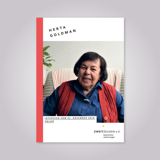 Eine alte Frau mit schwarzem Haar sitzt auf einem Sessel. Sie trägt eine blaue Bluse und eine rote Weste. Sie lächelt in die Kamera.